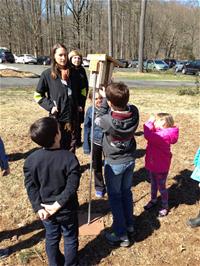 A group of children with an adult circled around a bird box